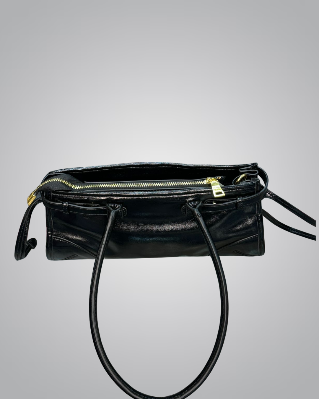 Black leather handbag with a gold zipper on a gray background
