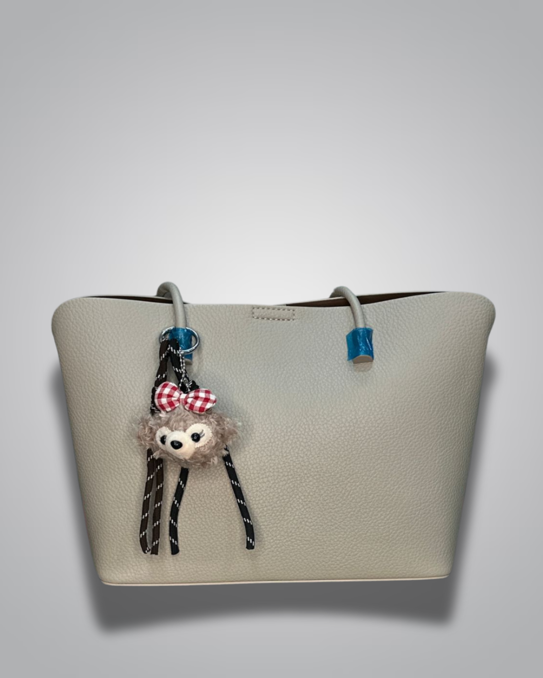 Beige handbag with a sloth keychain on a light gray background- Valentino Impex