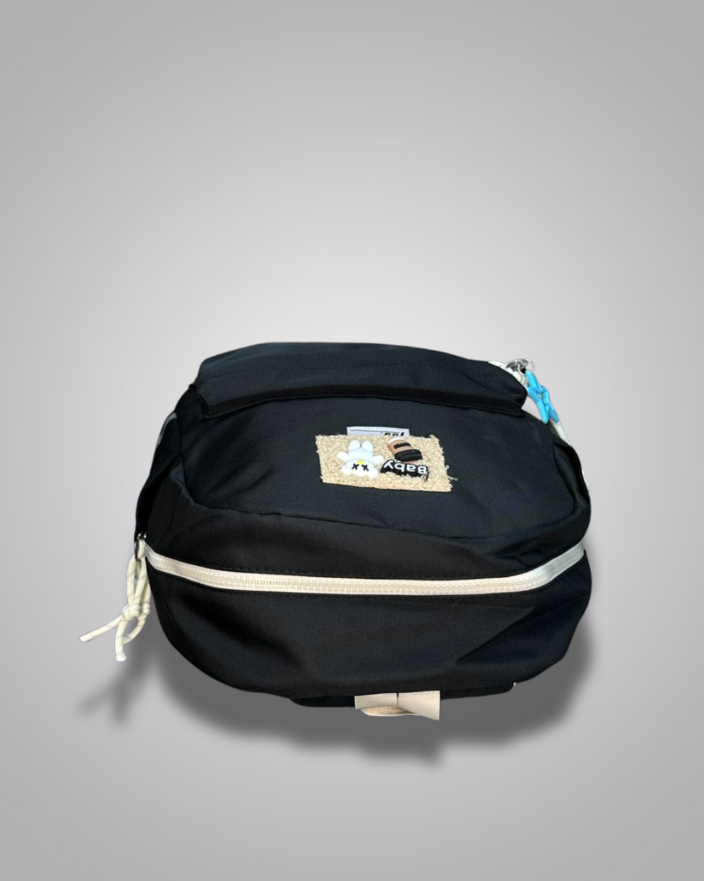 Black backpack with decorative patches and a blue star charm on a gray background- Valentino Impex