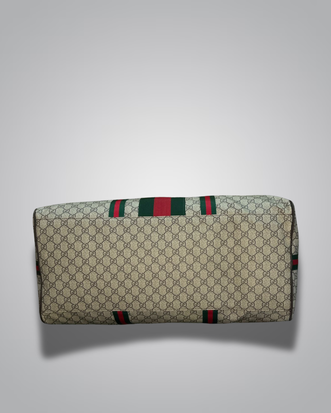 Designer handbag with monogram pattern and red and green stripes on a light gray background