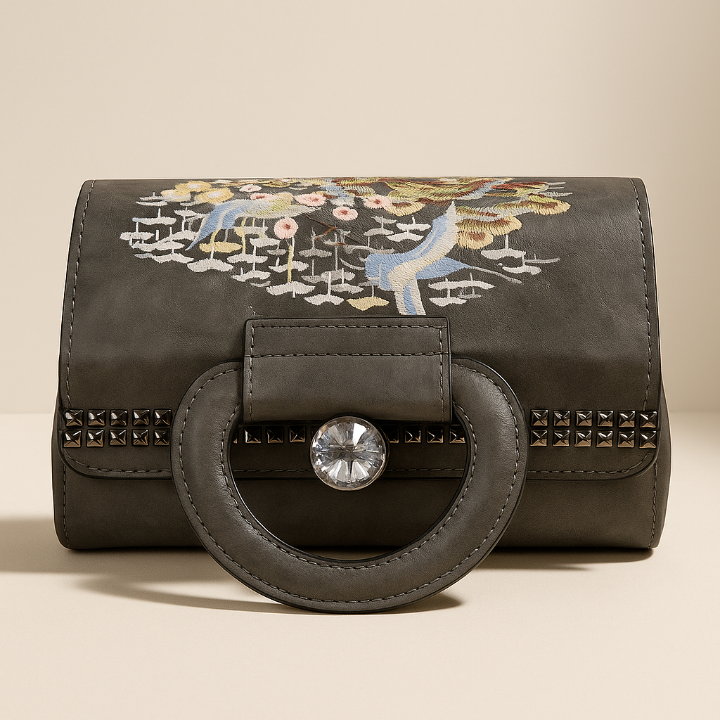 Black handbag with floral embroidery and studded details on a beige background